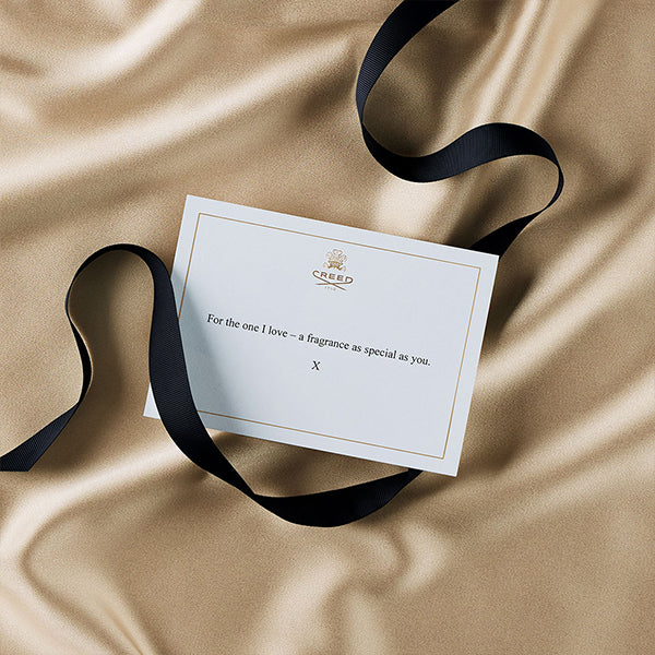 White gift message with gold embossed creed logo placed on a silk blanket